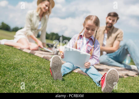 Kind mit digitalen Tablet während die Eltern hinter bei Picknick sitzen Stockfoto