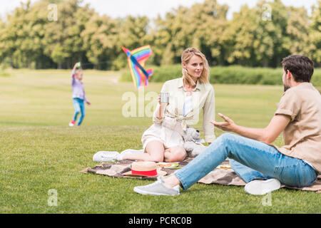 Eltern in Plaid bei Picknick sitzen während hinter Tochter in Park Stockfoto