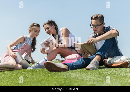 Low Angle View von lächelnden Jugendlichen studieren mit Büchern und digitalen Tablet in Park Stockfoto