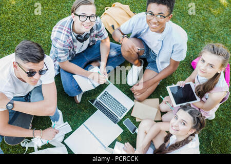 Hohe Betrachtungswinkel von Happy multiethnischen teenage Studenten studieren mit Bücher und digitale Geräte in Park Stockfoto