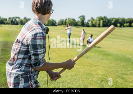 Seitenansicht von Teenage boy Holding Baseball Schläger und spielen mit Freunden im Park Stockfoto