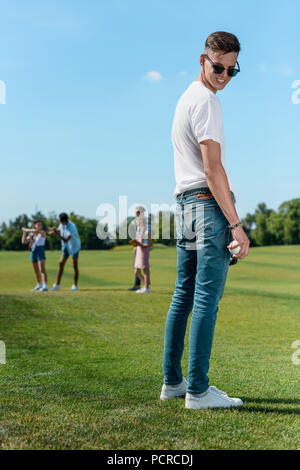 Lächelnd Teenager in Sonnenbrille spielen Baseball mit Freunden im Park Stockfoto