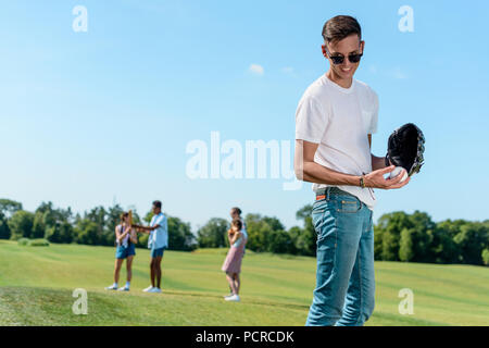 Lächelnd Teenager Junge spielt Baseball mit Freunden im Park Stockfoto