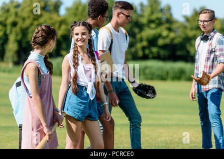 Happy teenage Freunde mit Bücher und Rucksäcke spielen Baseball in Park Stockfoto