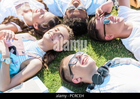 Hohe Betrachtungswinkel von Happy multiethnischen Teenager Freunde zusammen liegen auf der grünen Wiese Stockfoto