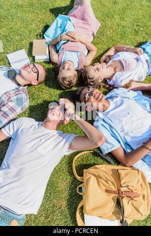 Hohe Betrachtungswinkel von Happy teenage Freunde mit Bücher und Rucksack liegen auf Gras Stockfoto