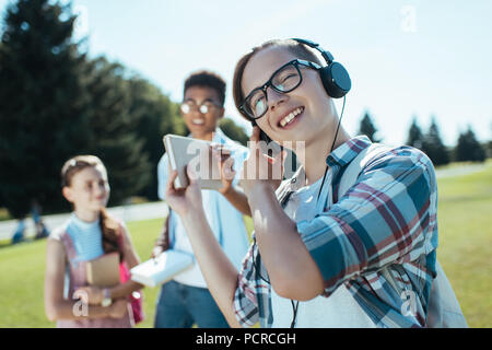 Lächelnd Jugendlicher in Kopfhörer Buch geben an Freund im Park Stockfoto