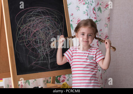 Kind ist das Zeichnen mit Farbe Chalk auf der Kreidetafel. Mädchen ist Ausdruck von Kreativität und Blick in die Kamera. Konzept der Ausdruck und Lernen Stockfoto