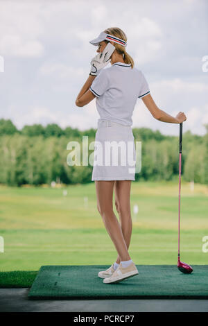 Seitenansicht der weiblichen Golf Spieler in Polo und Kappe mit Golf Club in der Hand sprechen auf dem Smartphone am Golfplatz Stockfoto