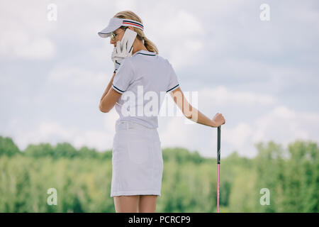 Seitenansicht der weiblichen Golf Spieler in Polo und Kappe mit Golf Club in der Hand sprechen auf dem Smartphone am Golfplatz Stockfoto