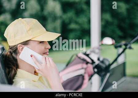 Seitenansicht der weiblichen Golf Spieler in Gap sprechen auf dem Smartphone am Golfplatz Stockfoto