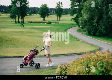 Seitenansicht der weiblichen Golf Spieler mit Golf Gear sprechen auf dem Smartphone beim Gehen auf Golfplatz Stockfoto