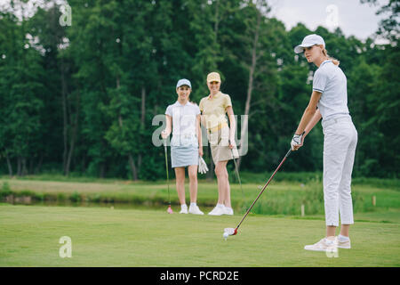 Selektiver Fokus der Frau in Gap, Golf zu spielen, während Freunde stehen in der Naehe Golfplatz Stockfoto