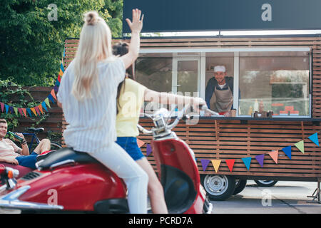 Rückansicht der Mädchen auf scooter Hand winken zu Koch in Essen Lkw Stockfoto