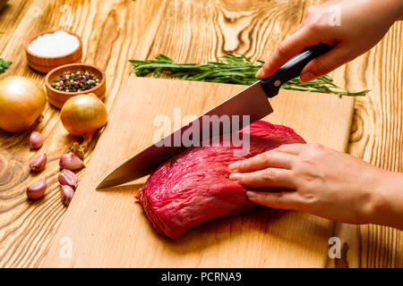 Frau Schnitte von frischem Fleisch in der Küche Stockfoto