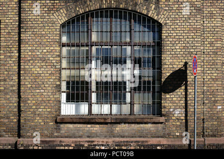 Ein stoppschild wirft einen Schatten auf die Wand auf dem stillgelegten Industriegelände von einer alten Fabrik mit einem vergitterten Fenster Stockfoto