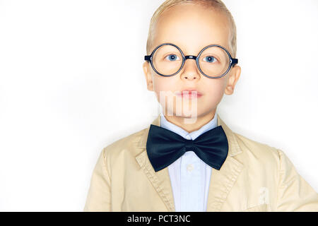 Adorable kleine blonde Junge, gekleidet wie ein Professor Brille trägt, einen Anzug und Fliege steht selbstbewusst vor einem weißen Hintergrund Stockfoto