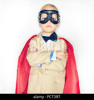 Adorable kleinen Jungen Superhelden in Anzug und Fliege trägt einen roten Mantel und Brille suchen mutige während vor einem weißen Hintergrund stehen Stockfoto