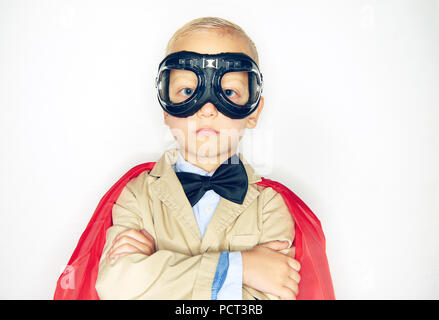 Süße kleine Junge Superheld in Anzug und Fliege tragen einen roten Umhang und Schutzbrille, fearless, während vor einem weißen Hintergrund stehen Stockfoto