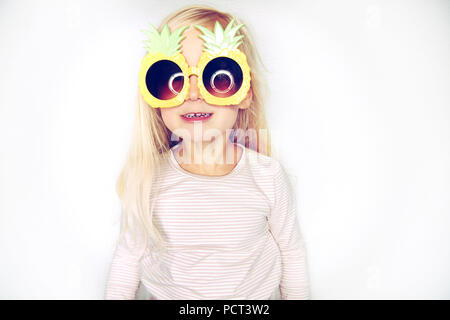 Süße kleine Mädchen mit langem, blondem Haar zu tragen lustig Ananas Sonnenbrille lächelnd und ein Gesicht vor einem weißen Hintergrund Stockfoto