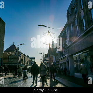 Käufer entlang eine High Street, Christmas shopping. Weihnachten Dekorationen Straße Lichter schmücken. Stockfoto