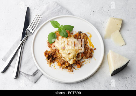Traditionelle Fleisch Lasagne mit Hackfleisch, Sauce Bolognese und Bechamelsauce in Weiße, runde Platte am grauen Stein Hintergrund Stockfoto