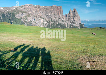 Europa, Italien, Bozen, Südtirol, Seiser Alm - Seiser Alm. Urige Hütten auf der Seiser Alm Wiesen und die Schatten einer Gruppe von Wanderer, im Hintergrund der Schlern, Dolomiten Stockfoto