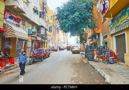 ALEXANDRIA, Ägypten - Dezember 18, 2017: Die schmale Straße der armen Karmouz Bezirk mit Tabellen der lokalen Teehäuser, in denen Besucher rauch Shisha und Abakus Stockfoto