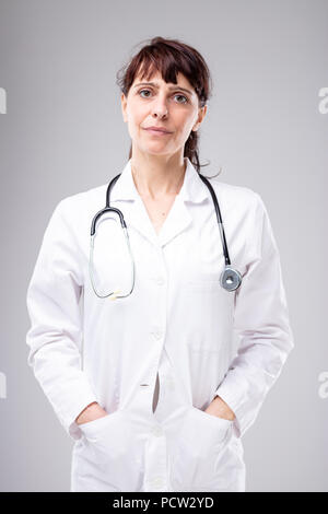 Mitfühlende Ärztin oder Krankenschwester mit einem Stethoskop um den Hals mit Händen in der Tasche ihres weißen Lab oat wohlwollend suchen Stockfoto