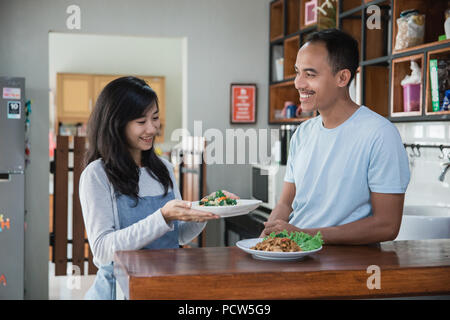 Schöne asiatische Frau in der Küche mit Ehemann die Zubereitung von Speisen zum Mittag- Stockfoto