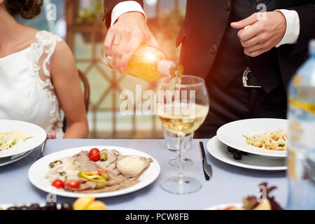 Horizontale Nahaufnahme der kaukasischen Mann im schwarzen Anzug und weißes Hemd gießen Rose Wein in ein hohes Glas aus der Flasche Stockfoto