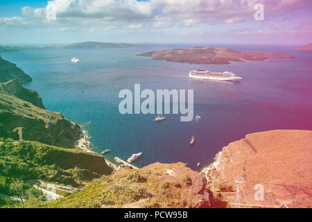 Wunderschöner Blick über die Ägäis von Fira auf Santorini, Griechenland. Kreuzfahrt Schiffe, Boote und die Caldera können im tiefen blauen Meer gesehen werden. Farbiges Licht Undichtigkeit Filter angewendet. Stockfoto