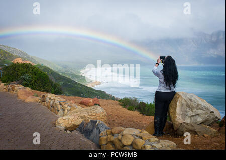Frau unter Foto von malerischen Blick auf Regenbogen über Sandstrand in Kogel Bay, Western Cape Provinz, in Südafrika. Stockfoto