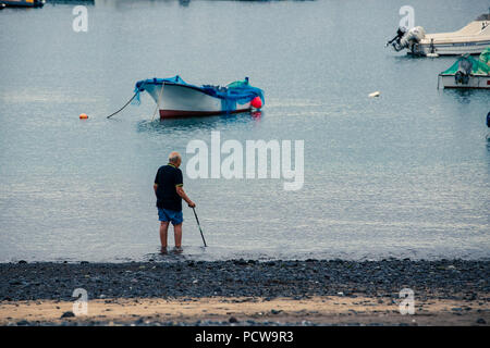 Alter Mann mit Stock, seine Füße an der Küste des Meeres in der Nähe der Boote im Hafen genießen. Stockfoto