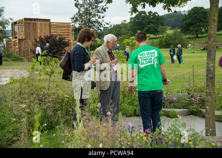 Menschen sehen zentrales Merkmal Baum, gepflasterten Bereich und Blumen im Garten, schöne Show - Macmillan Erbe Garten, RHS Chatsworth Flower Show, England, UK. Stockfoto