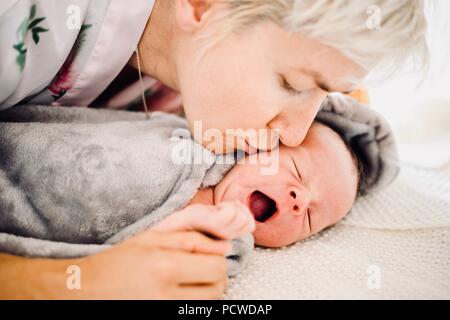 Mutter küssen ihr Gähnen oder Weinen neugeborenes Baby Boy Stockfoto