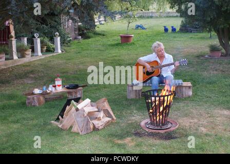 Mit der Gitarre in der Hand, die Frau singt am Lagerfeuer Stockfoto