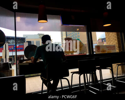 Ein Mann, der allein an einer Theke in einem Café sitzt und durch ein großes Panoramafenster in Ontario, Kanada, blickt. Beobachten Sie, wie die Welt vorbei geht. Einsamkeit. Allein. Ich Stockfoto