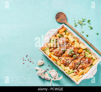 Chicken Drumsticks mit Gemüse in backen Auflauf auf hellblauem Hintergrund mit Kochlöffel und Kräuter und Gewürze, Ansicht von oben mit der Kopie Raum Stockfoto