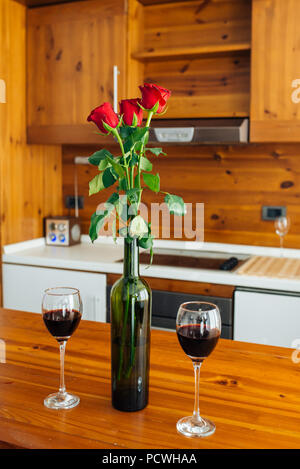 Drei rote Rosen in der Flasche und zwei Gläser Rotwein auf dem Tisch Stockfoto