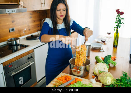 Attraktive Frau im blauen Kleid Bereitet Köstliche Spaghetti essen in der Küche Stockfoto