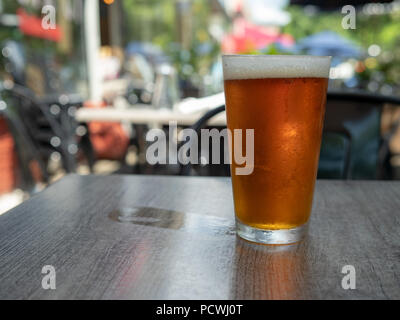 Ice Cold Bernstein Bier sitzen in einem Pint Glas auf einem Tisch draußen mit nassen cup Ring Stockfoto