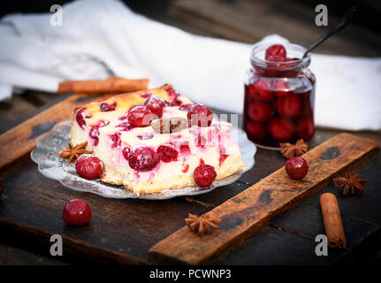 Stück Käsekuchen mit Kirschen auf einer Glasplatte und einen Krug mit marinierten Beeren Stockfoto