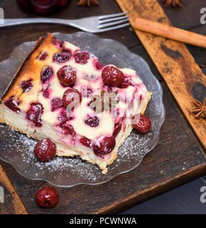 Stück Käsekuchen mit Kirschen auf einer Glasplatte und Eisen Gabel auf einem braunen Holztisch Stockfoto