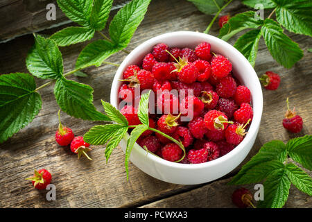 Frische süße Himbeeren in eine keramische Schüssel auf einen hölzernen Tisch. Das Konzept der Ernährung für Superfoods und Gesundheit oder Entgiftung. Stockfoto
