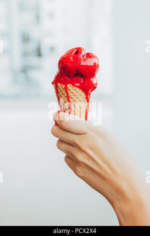 Woman's Hand mit einem erfrischenden und appetitlich Kegel von Himbeere Eis, das Eis langsam schmilzt in der Hitze des Sommers Stockfoto
