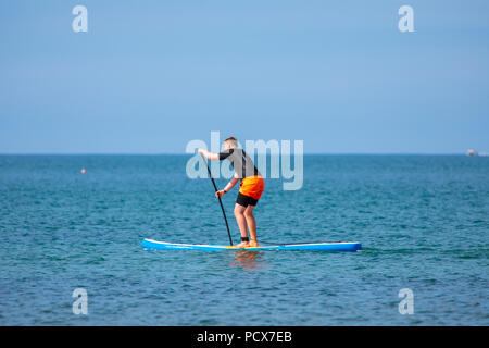 North Wales, 4 UK Wetter: Warme, sonnige Wetter kehrt in vielen Teilen der britischen dieses Wochenende, wie diese Person entdeckt Paddle Boarding über den ruhigen Gewässern rund um Kirche Bay auf Anglesey, Nordwales Stockfoto