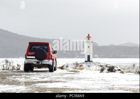 Rotes Auto vor dem Leuchtturm an der Küste in schneereichen Winter Tag Stockfoto