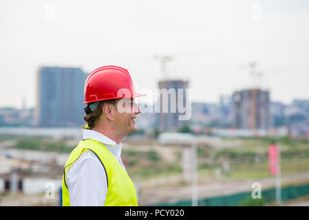 Ingenieur auf einer Baustelle tragen gelbe reflektierende Westen und Roten Helm mit Gebäuden und Krane im Hintergrund. Polier auf der Baustelle Stockfoto