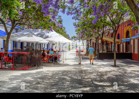 Ayamonte, Spanien - 20. Juni 2018. Touristen und Einheimische genießen Sie den Schatten des hübschen Jacaranda-bäume auf der Plaza La Lota. Einige von ihnen sind im Freien Stockfoto